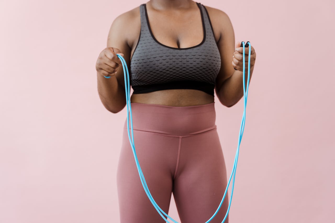Close-up of a woman in activewear holding a jump rope against a pink background.